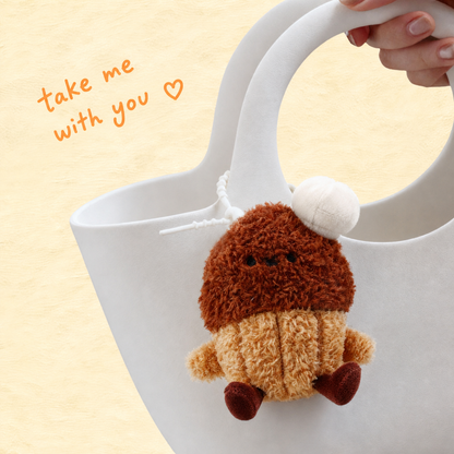 KUKI brown muffin plush gel pen keychain hanging from a white handbag